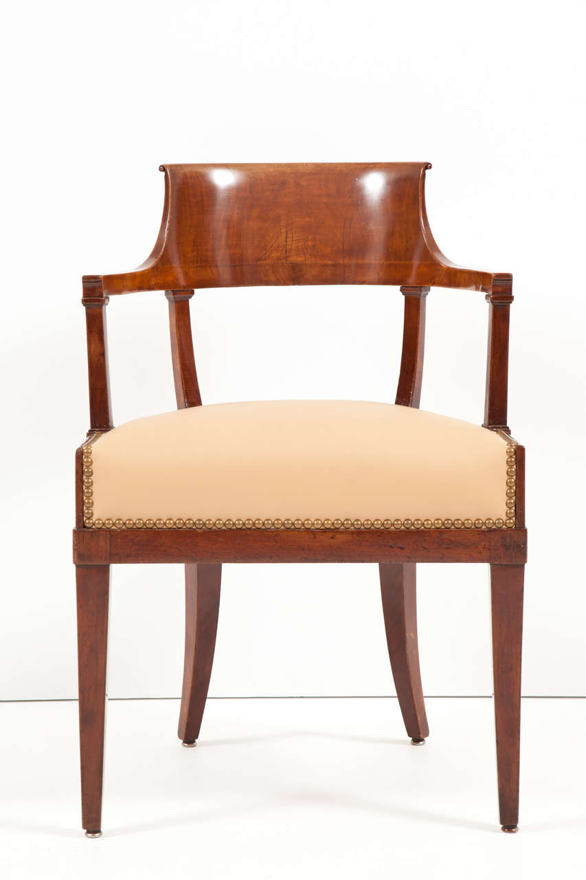 A Swedish mahogany neoclassical open armchair, early 19th century, with a scrolled and curved backrest, above a wide frieze and upholstered seat, on square tapering legs.