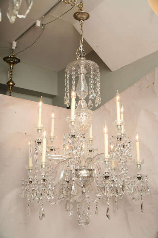An English George II style two tiered 12 light chandelier with S shaped crystal arms and cut crystal star shaped bobeches having crystal drops and strands of draped crystal beads from arm to arm.