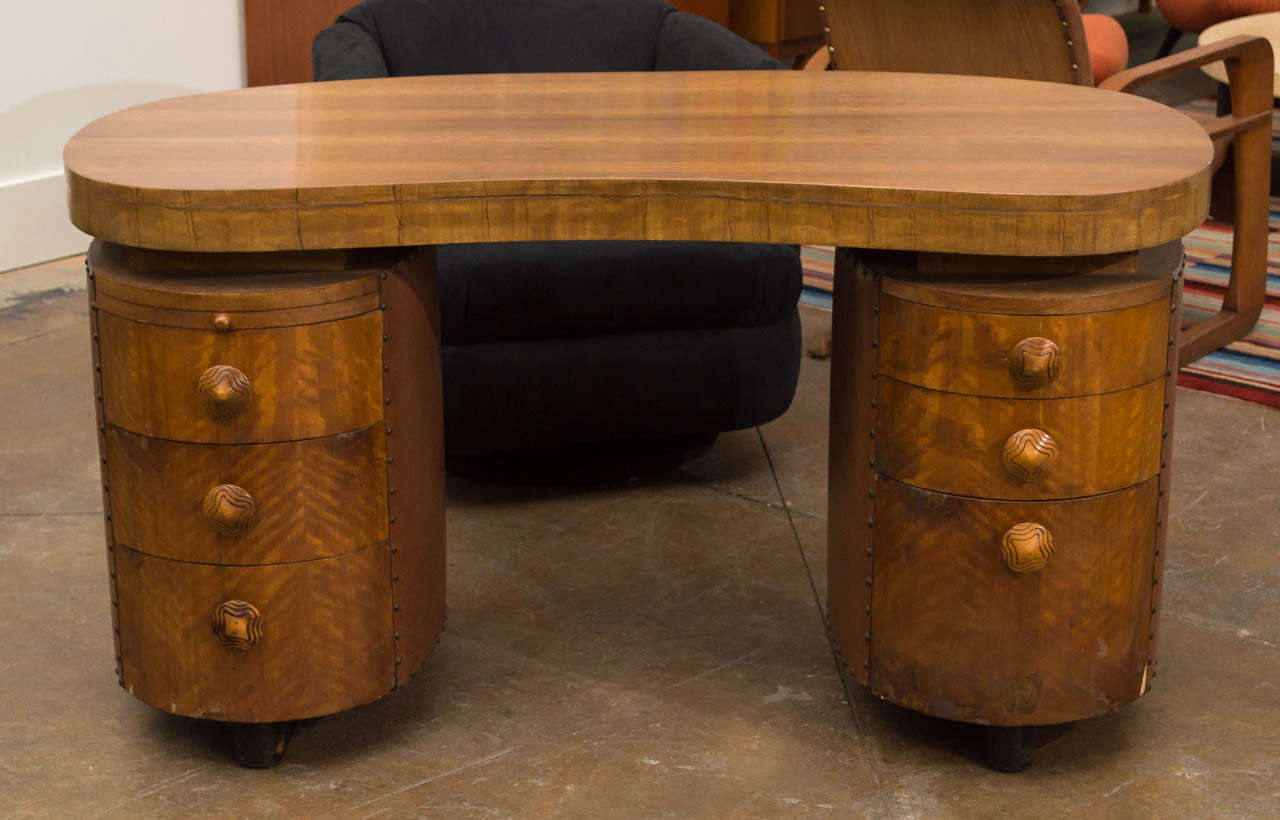 An amorphous desk of walnut with two oval cases of drawers under both sides. Both cases of drawers are wrapped in leather and lined with brass nailhead trim. There are six drawers of varying depth with a pull-out writing surface on the top left.
