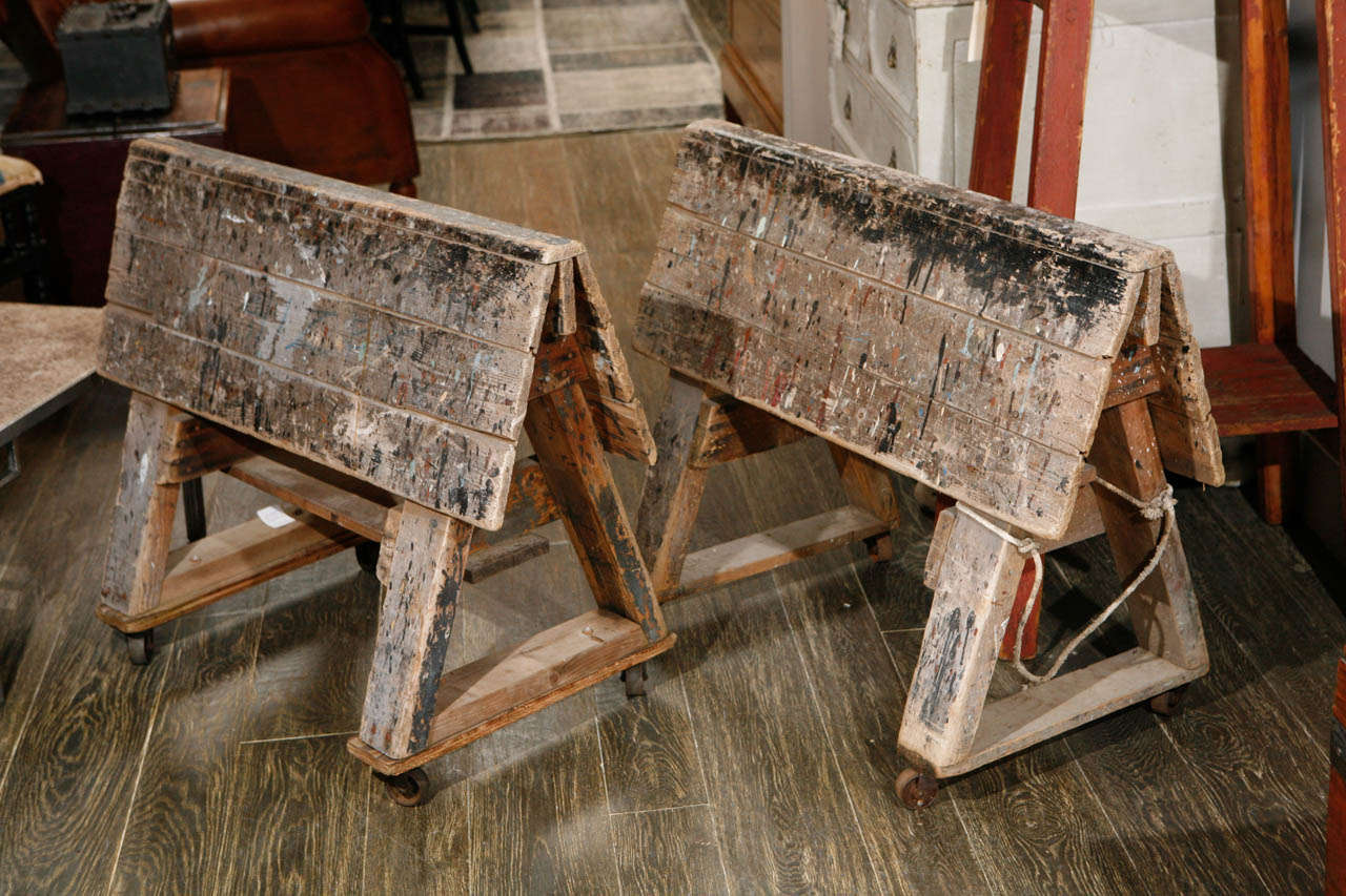 A pair of rolling wooden saw horses with paint that can be converted to a table or writing table.