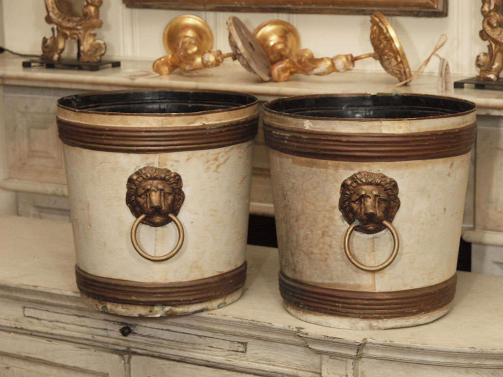 A pair of English 19th century white painted jardinières with golden lion heads. The jardinières are embellished with golden rings at top and bottom of the pots.