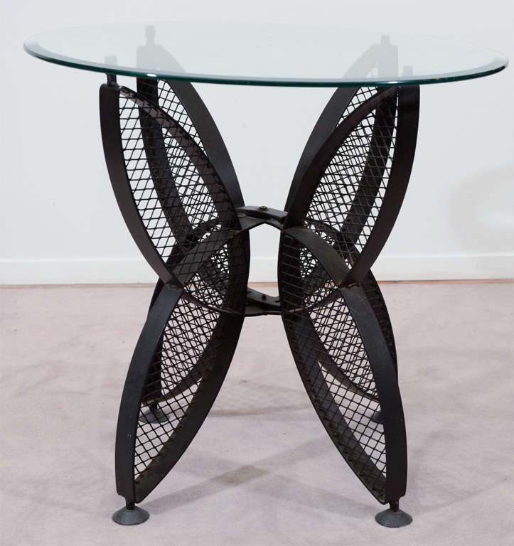 A single side table with a round glass top and a latticework iron base.