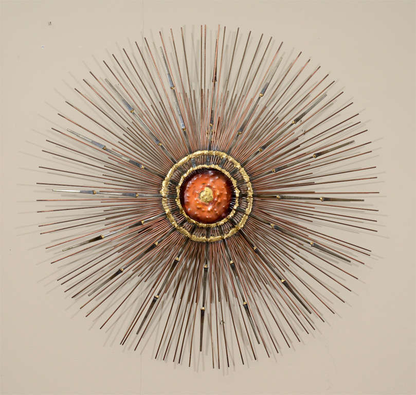 A star burst form wall sculpture with copper colored center and radiating metal 