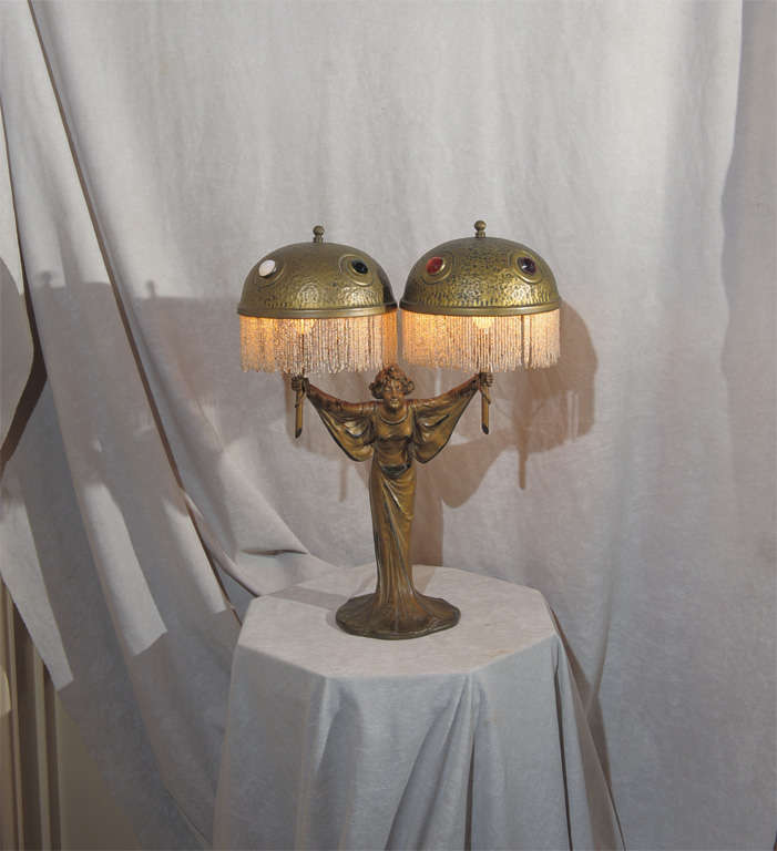 This graceful little lamp offers a nice example of the art nouveau period.  The attractive young gal is holding two original brass shades with faceted jewels and original glass beading.  A great mood lamp for any setting.