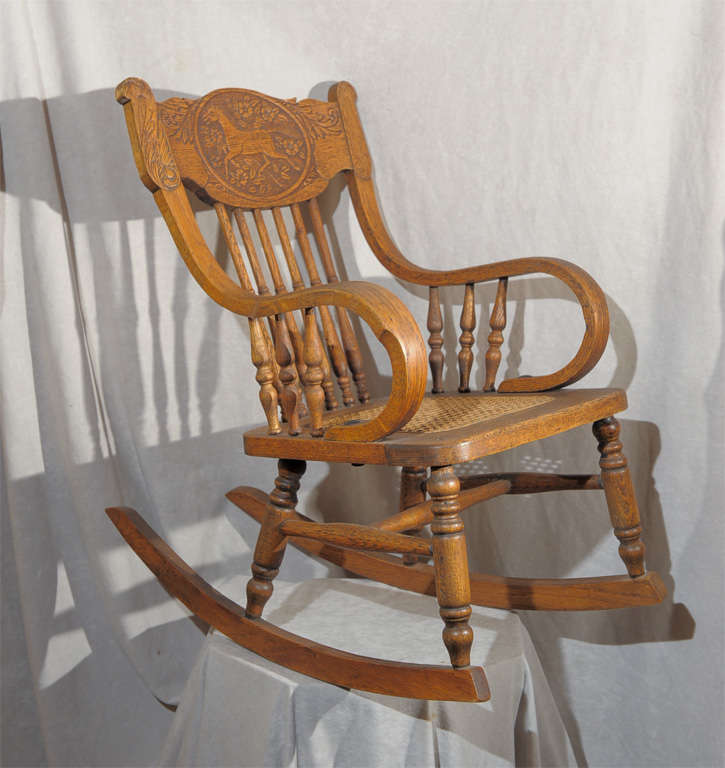 What a wonderful piece of child's furniture we have here.  This beautiful bent arm rocking chair has a detailed horse pressed into the back.  Note the lovely turned spindles and rich color.  Nice cane seat for comfort.  We've sold a lot of oak