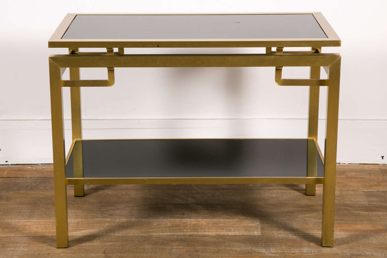 A pair or two tiers varnished brass tables , black opaline tops ; by Guy Lefevre for Jansen . circa 1970 .