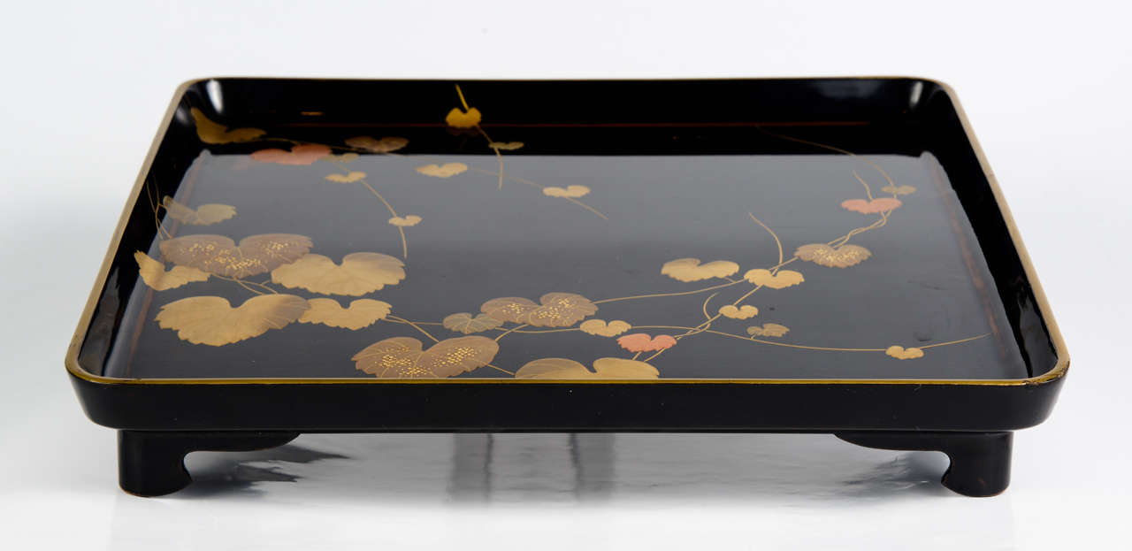 Japanese lacquer tray with black background decorated with polychrome lacquer leaves. Back in black lacquer. The tray rests on four feet.