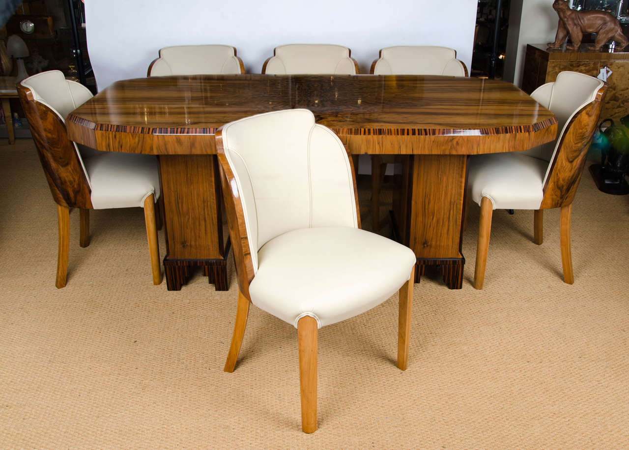 An Art Deco dining table and six walnut backed cloud form chairs, attributed to Harry and Lou Epstein. Figured walnut with Macassar ebony banding, walnut pedestals with stepped Macassar ebony feet. Chairs upholstered in rich cream