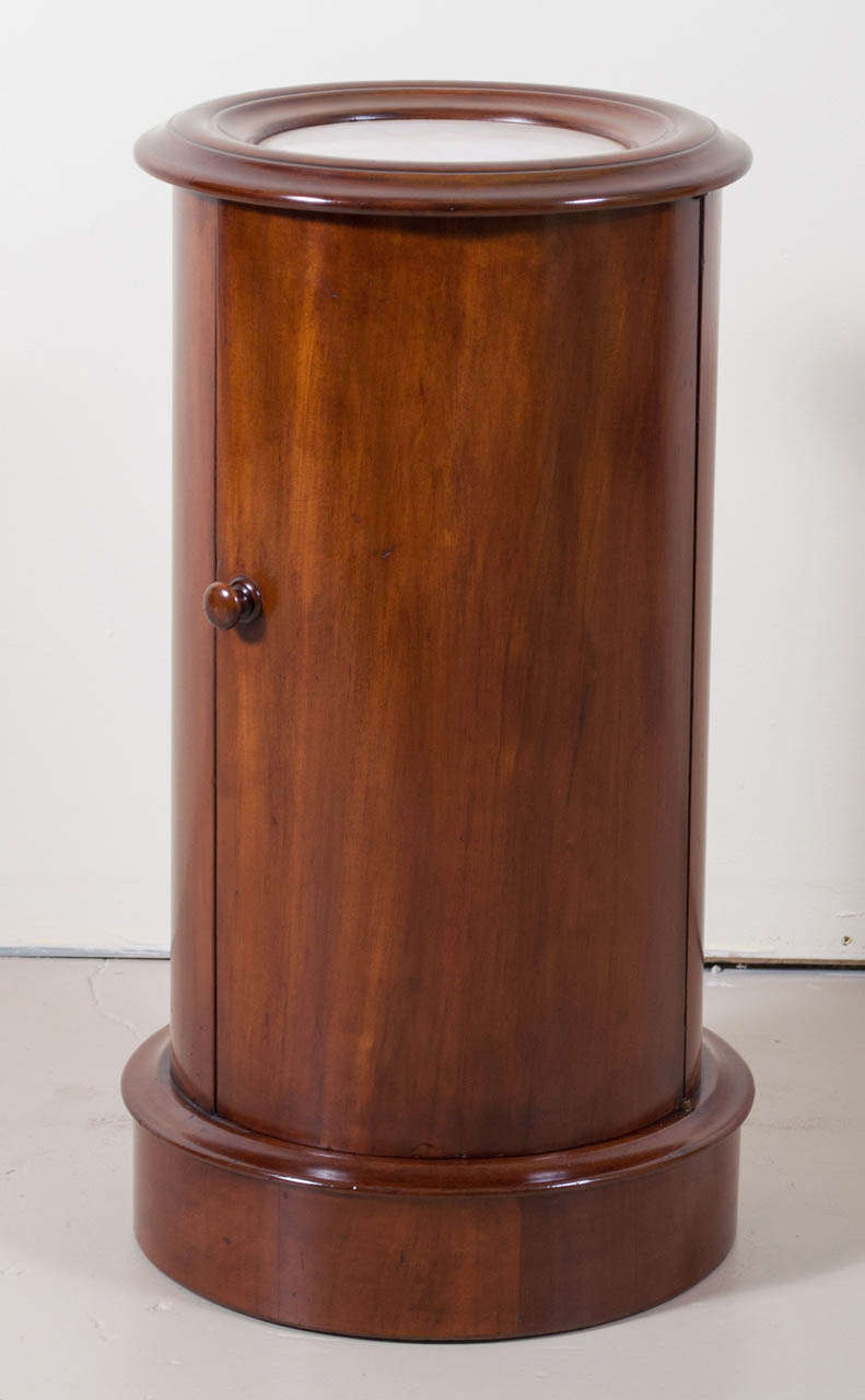 A gorgeous Victorian Mahogany Cylinder Pot Cupboard. The molded top has a white marble insert above an arched swinging cabinet door opening to a conforming shelf.  The Pedestal is raised on a circular plinth base. This Cupboard retains its
