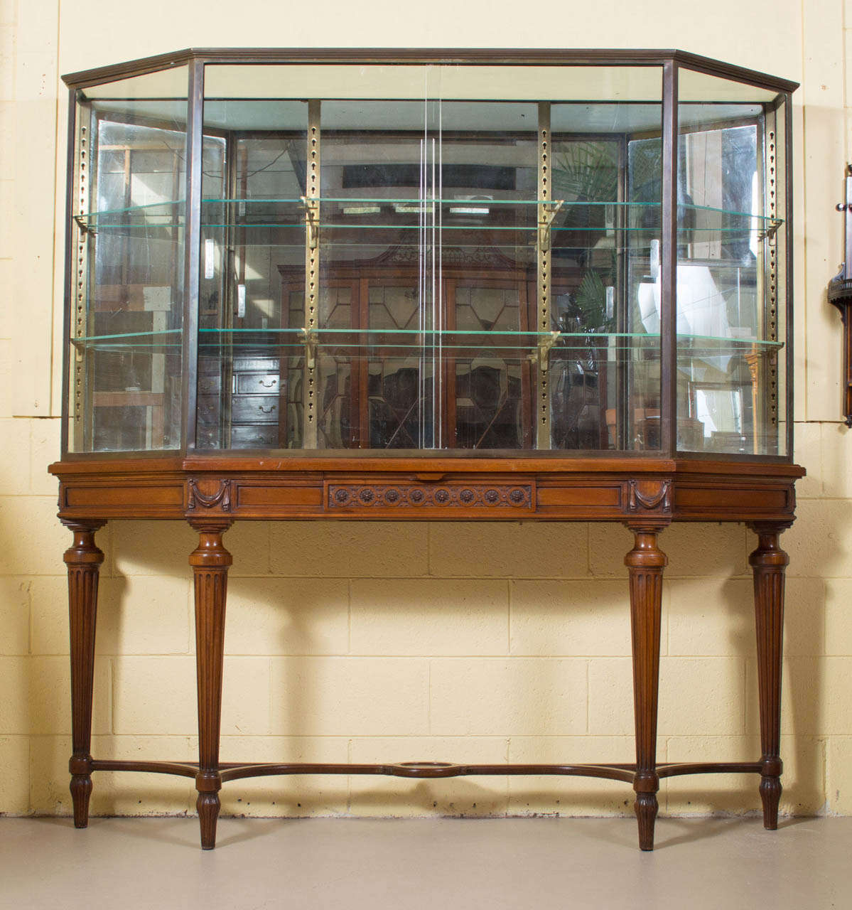 A unique carved walnut Louis XVI style two-part vitrine. The upper portion is a brass and glass display cabinet with two sliding glass doors. The interior has two adjustable glass shelves and a mirrored back. The carved walnut base is raised on four