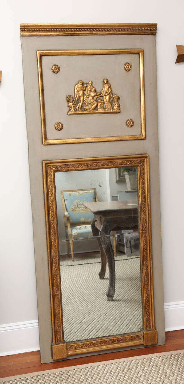 A painted and parcel-gilt trumeau mirror of exceptional quality. The upper portion displays a raised mythological scene surrounded by a molded frame and four rosettes. The lower portion is a beautifully crafted giltwood frame with a lovely floral