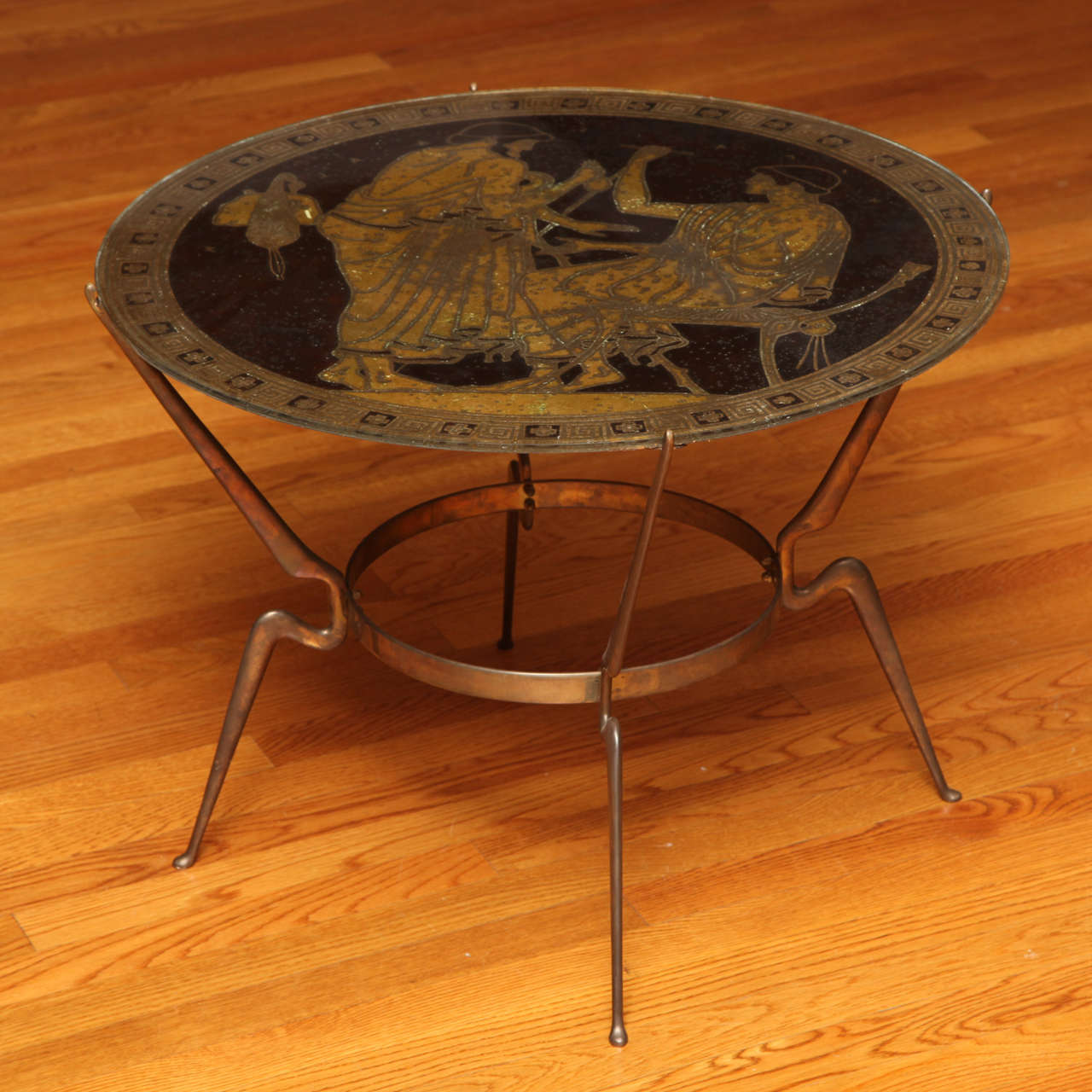 The round verge églomisé top depicting two classical figures in gold on a Coco-Cola brown ground; set onto a gilt metal base with four legs joined by a round stretcher.
