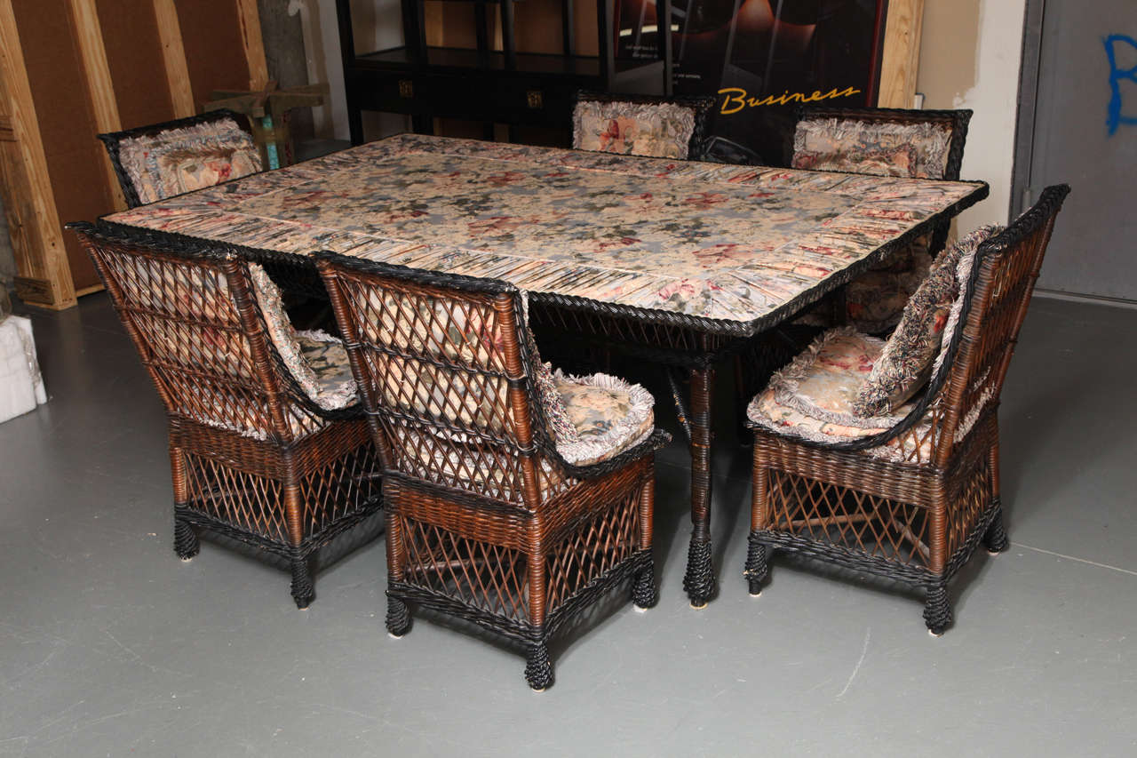 Comprising six side chairs and a dining table with upholstered textile insert beneath a glass plate top. Very early set in natural and black stained finish. With excellent condition with minor losses.

Provenance: Antique American Wicker, Nashua,