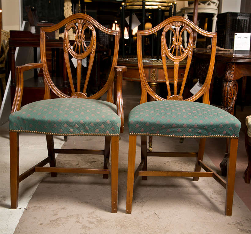 Set of 10 Sheraton style walnut dining chairs, circa 1920s, the set consists of two armchairs and eight side chairs. The shield-like back decorated with intricately carved plumes and ribbon, leading to a padded seat with nail-head, raised on squared