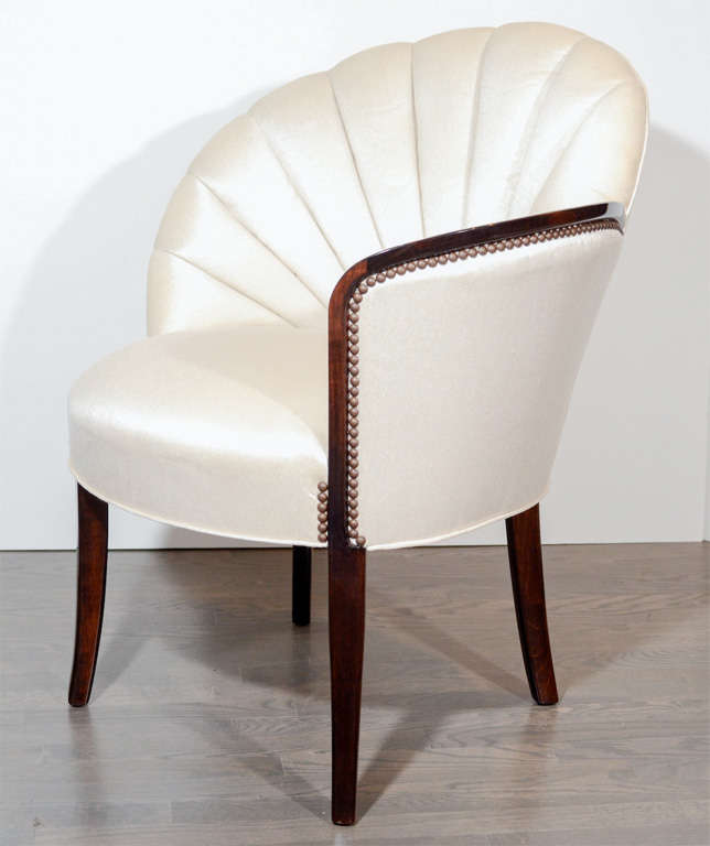 These gorgeous chairs epitomize the Hollywood era and glamour. They feature a tufted shell back design with ebonized walnut legs and arm and antique brass stud detailing. Newly upholstered in a creme sharkskin fabric.