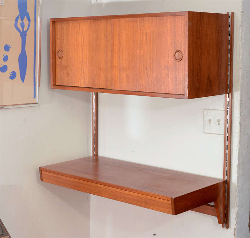 Handsome, practical, and versatile Danish wall mounted teak desk.  The wall unit is adjustable ( the height given below is as shown but can be adjusted ). The desk has a drawer and the teak cabinet above has storage and a pull out tray.