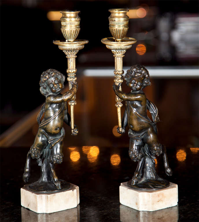 A pair of fine bronze candlesticks with faun mounted on animal legs carrying an ormolu torch in its arms..  French.