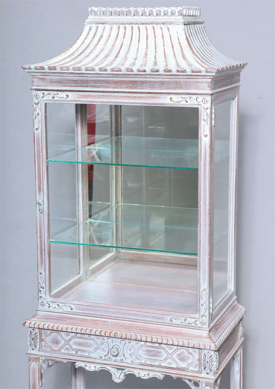 Display cabinet, of pickled mahogany, having glass sides and door, surmounted by a pagoda roof with pierced gallery on stand  with single frieze drawer decorated by fretwork, raised on fielded square legs joined by shelf stretcher.<br />
<br
