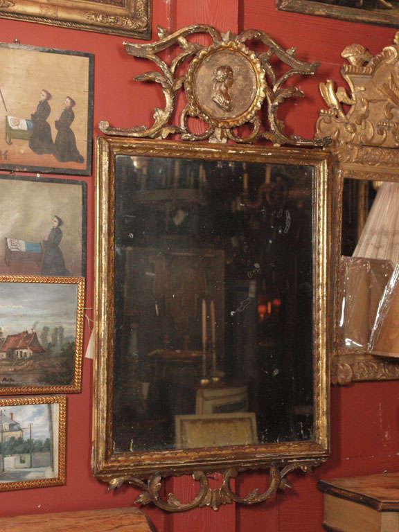 A Louis XVI Italian Mirror in a gilt frame. Top cartouche with a maiden's profile surrounded by various branch type carvings repeated at the bottom of the frame