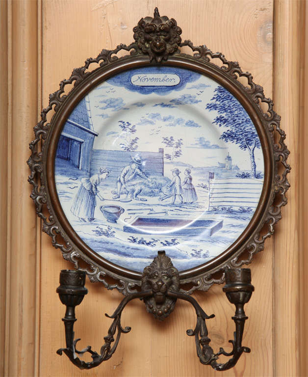 Each round plate painted with a scene depicting slaughter of a boar in front of house in blue. A man, woman and two children in a farmyard with a barn to the left. Inscribed 'November', from series of the months.of European figures in a farm setting