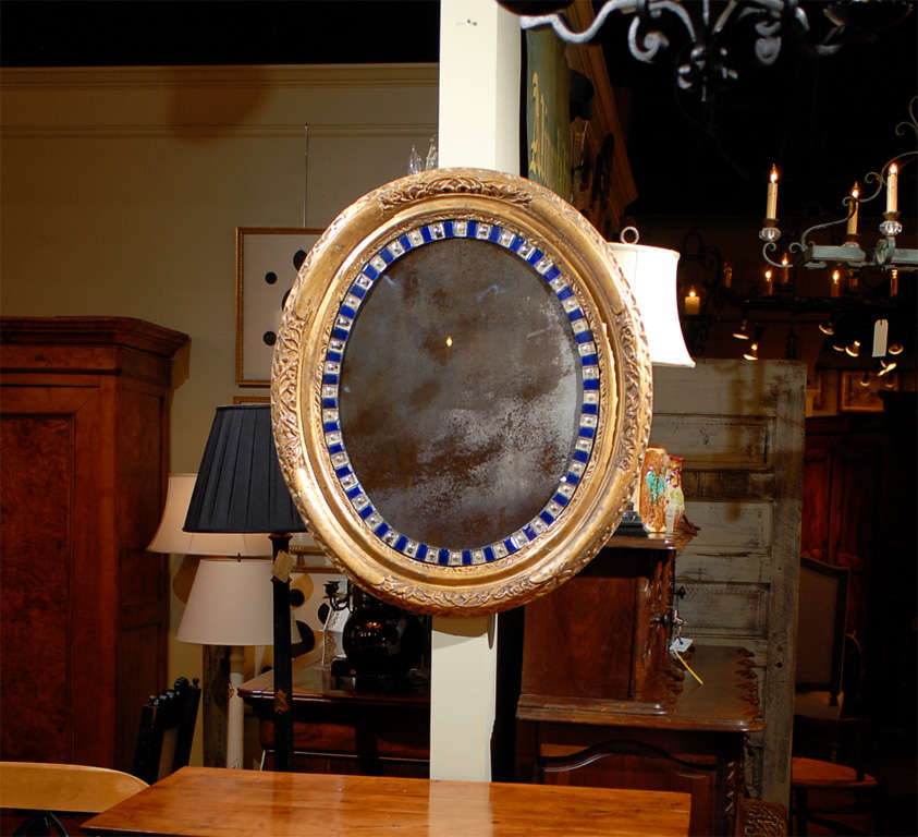 An Irish oval mirror with carved giltwood frame and blue and translucent cut glass border from the 19th century. This medium size mirror features an oval gilded frame with low-relief carved foliage accents in the four main directions, beautifully