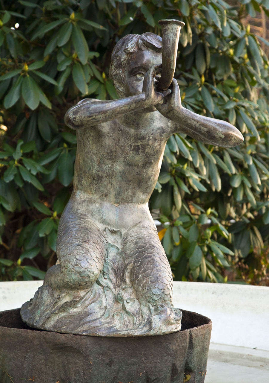A metal fountain figure of a seated merboy blowing a horn, verdigris patina, piped for water.