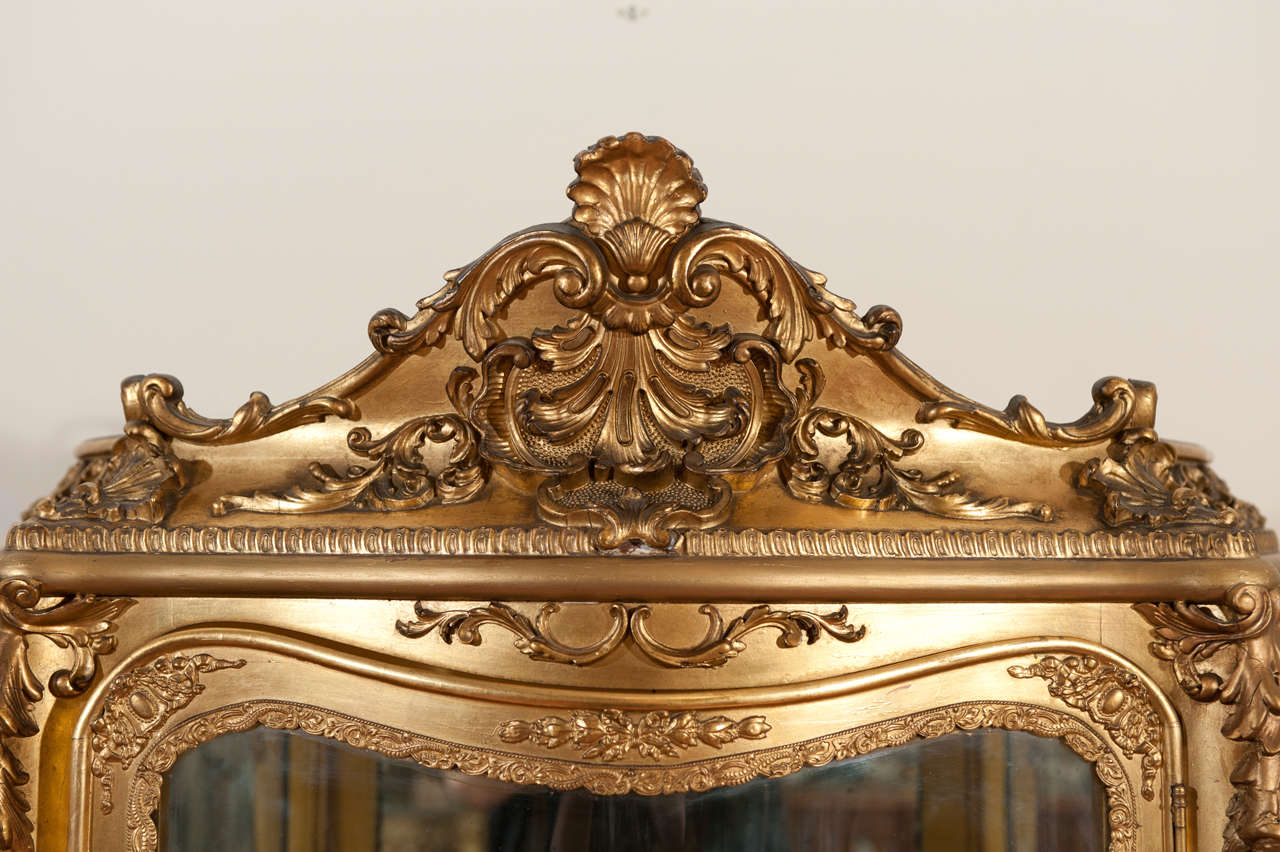 Louis XV style gilded vitrine with Vernis Martin painted galant scenes on tree lower side of the vitrine. Extensive hand carving on the entire piece, mirrored back , two glass shelves and  gold velvet on lower shelf.