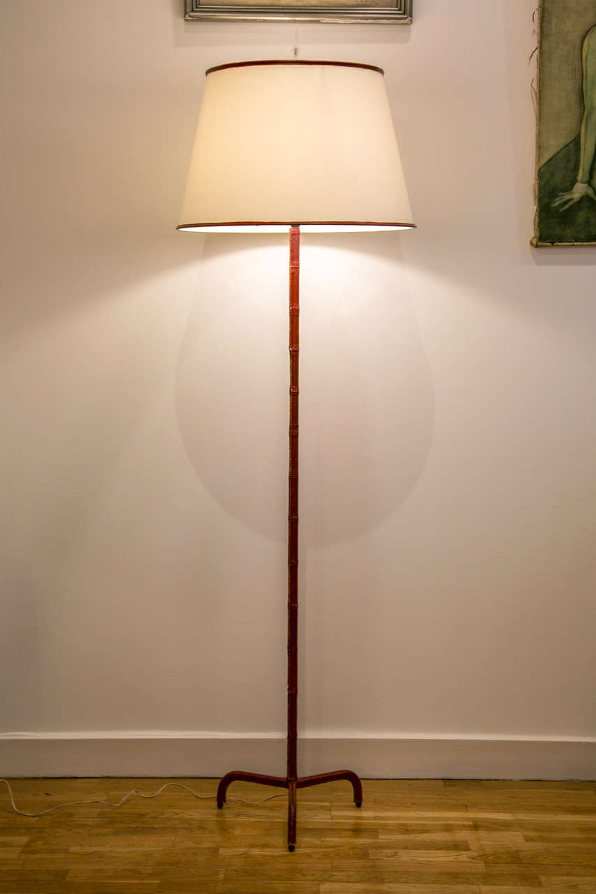 Floor lamp with tripod base by Jacques Adnet. Covered with saddle stitched Bordeaux red leather. Large white shade with blue leather piping.

Wired for European use.

A second slightly different lamp covered with dark blue leather is also