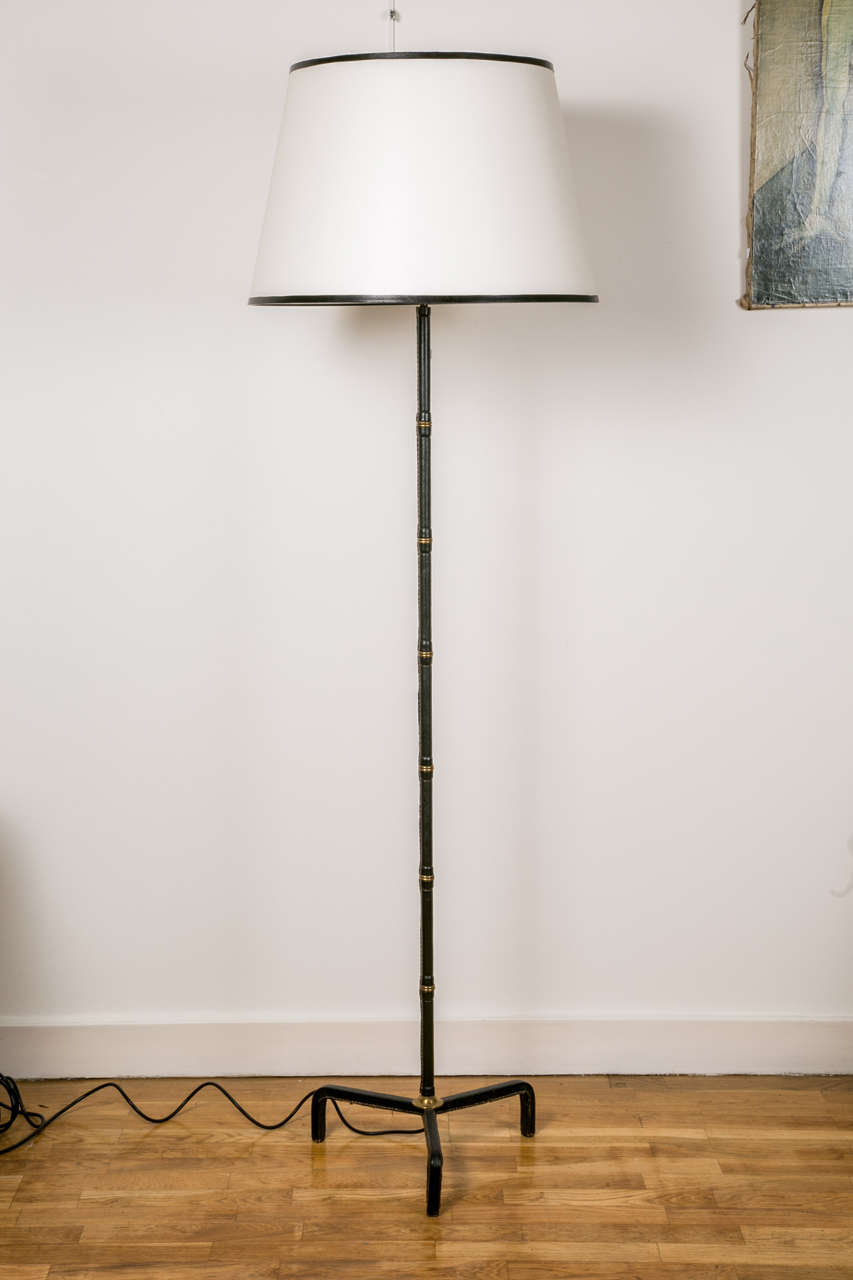 Floor lamp with tripod base by Jacques Adnet. Covered with saddle stitched dark blue leather. Brass rings on the trunk. Large white shade with blue leather piping.

Wired for European use.

A second slightly different lamp covered with red