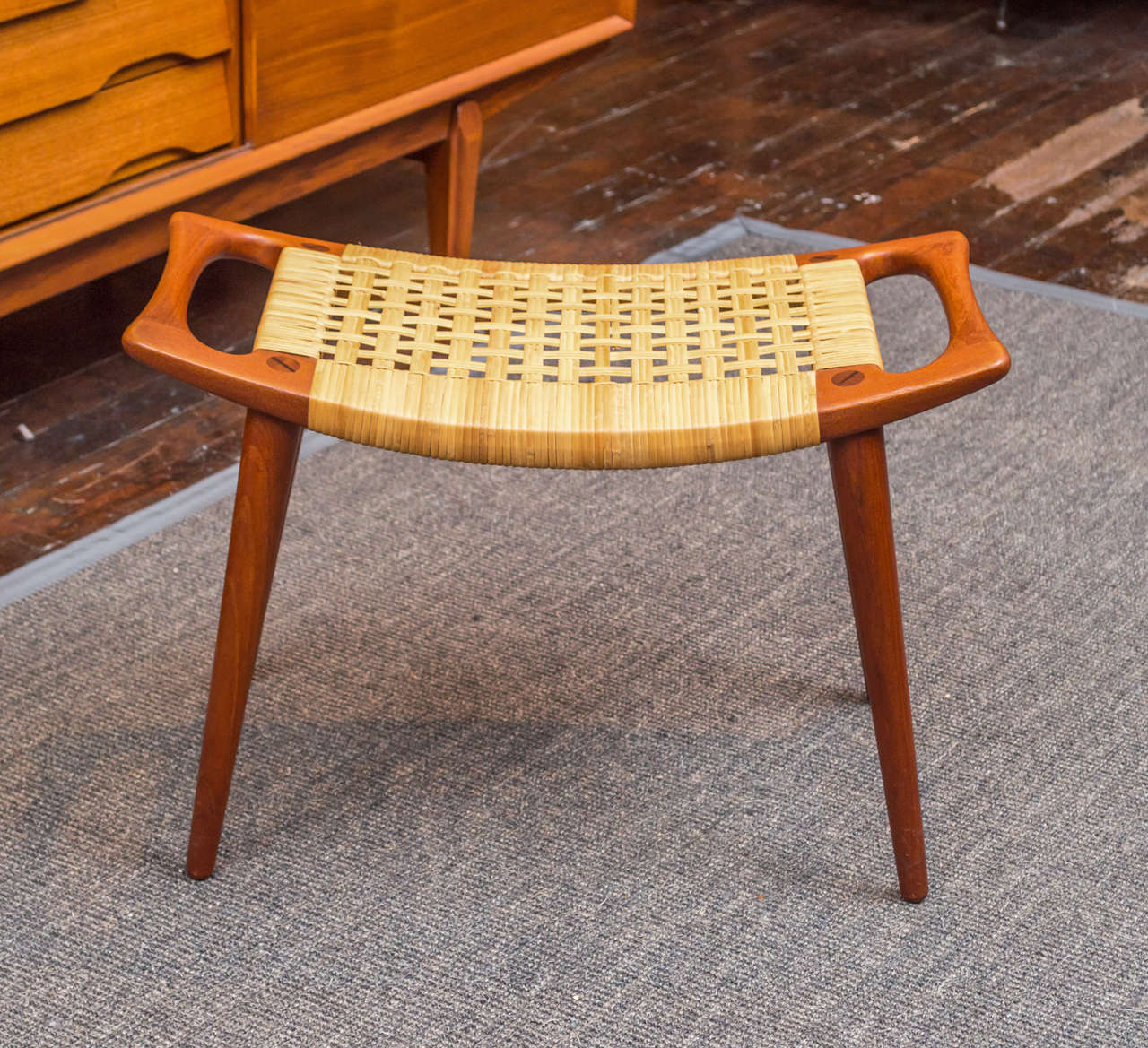 Sculptural stool or bench in excellent original condition. Made with solid teak and a woven cane seat. 
Made by Johannes Hansen, labeled.
