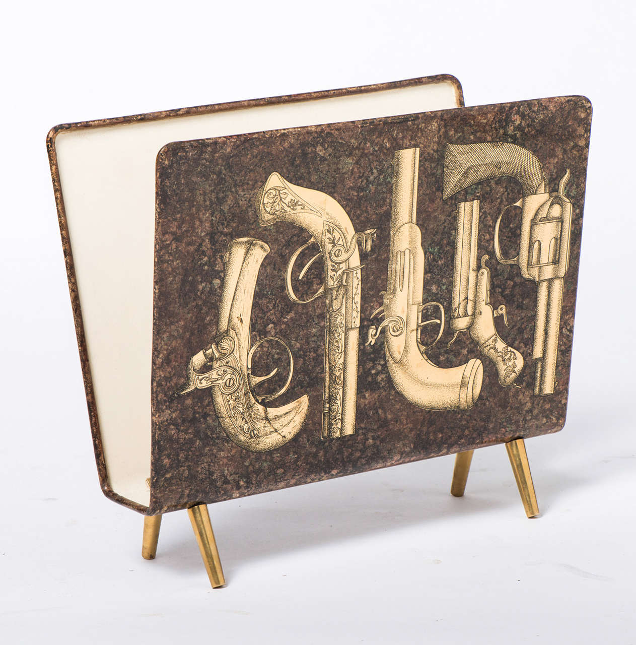 A Piero Fornasetti “Pistole” magazine Stand.
Lithographically printed and hand colored metal. 
Brass feet.
Italy, circa 1950.
Labeled.
Measures: 38.5 x 43 x 22.