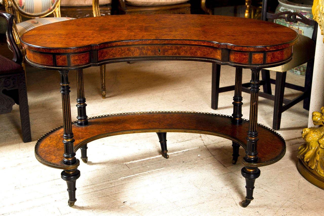 Kidney shaped burl amboyna and ebonized single drawer writing table. The lower shelf having a brass gallery.

The drawer stamped  Wright and Mansfield. Each leg ending in toupee type feet  with original casters.