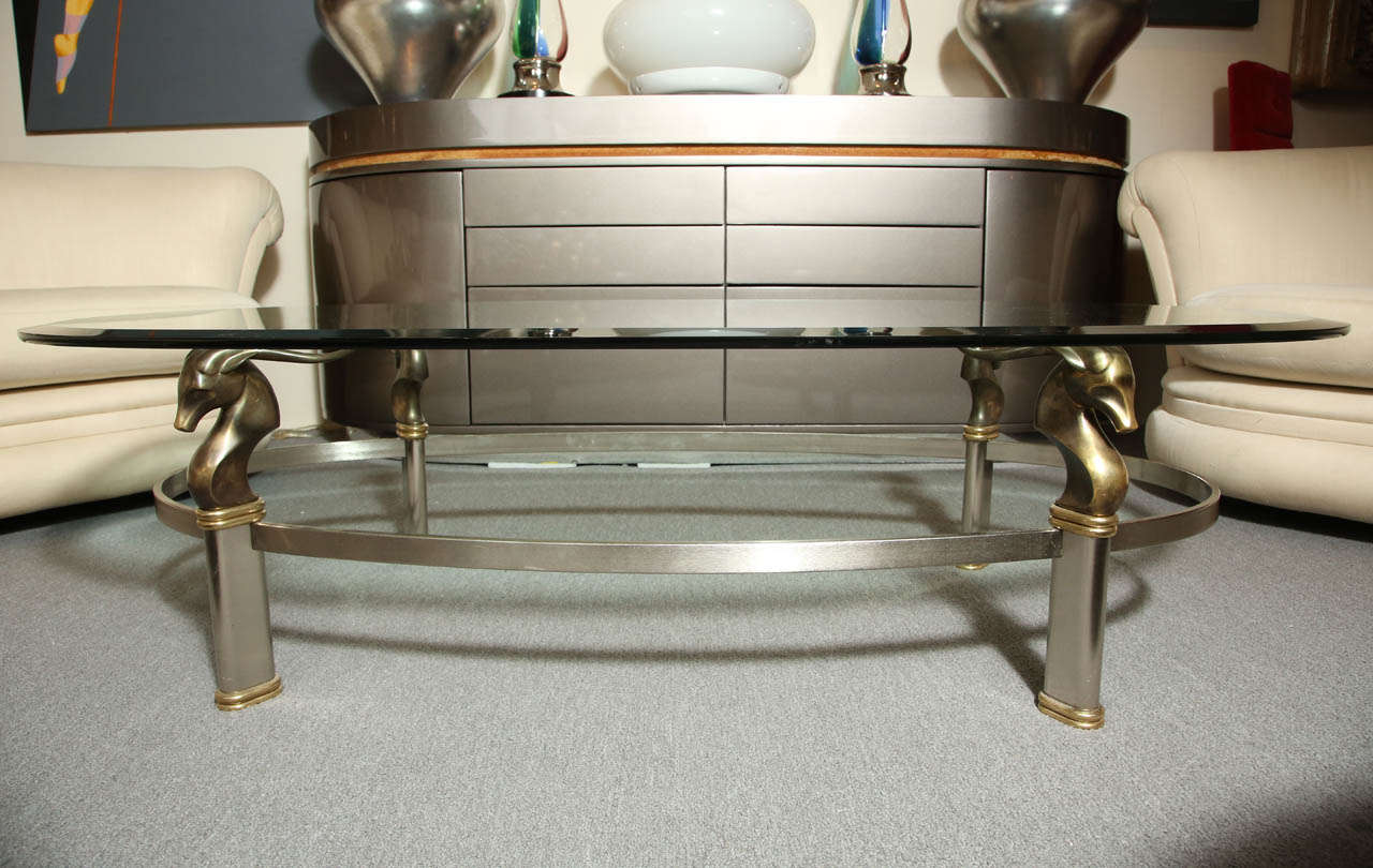 Exquisite oval glass coffee table with a steel base and bronze antelope heads which support the glass upon their horns.  The glass is beveled.
