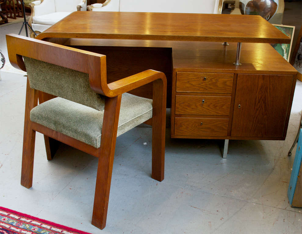 A Streamline Moderne desk and chair from the Czech Republic.
Desk and chair show nice graceful curves. Walnut veneer, base has been re-chromed. There's also a sliding glass door(s) cabinet on the front side of the desk, a perfect place to hold your