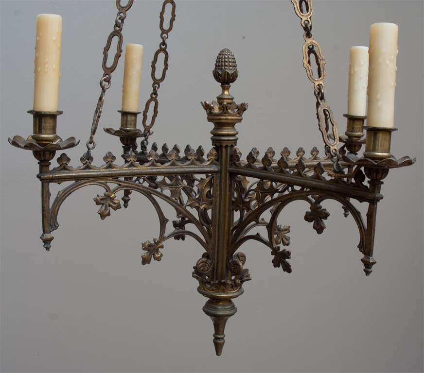 These unusual gilt brass Gothic style chandeliers each have four lights on cross arms. Top finials and bottom spikes all held by four chains leading to a top canopy, Arms have Gothic tracery and trefoil details. Chain may be shortened if desired.