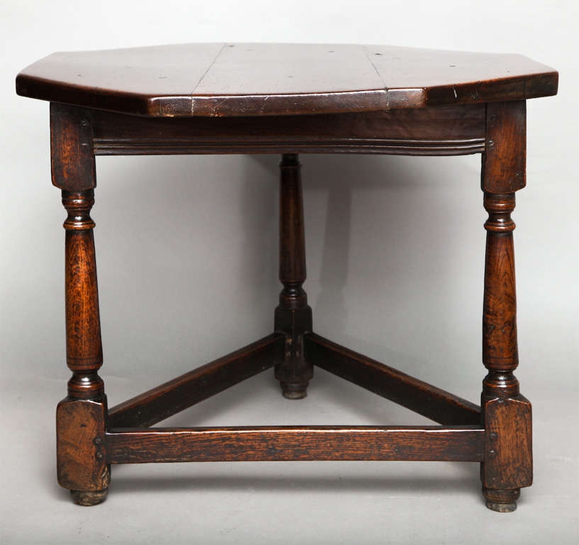 Rare 17th Century English oak cricket table, the thick plank top with scribed edges, over triangular base, the balustrade turned legs joined by stretcher base, standing on original bun feet, the whole with rich color and patination.