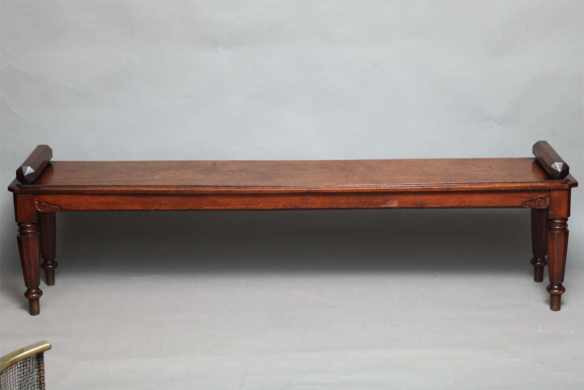 Most unusual George IV hall bench of impressive scale in beautifully patinated mahogany, the octagonal faceted bolster ends over single plank seat, the apron with carved foliate spandrels over faceted and turned octagonal legs.