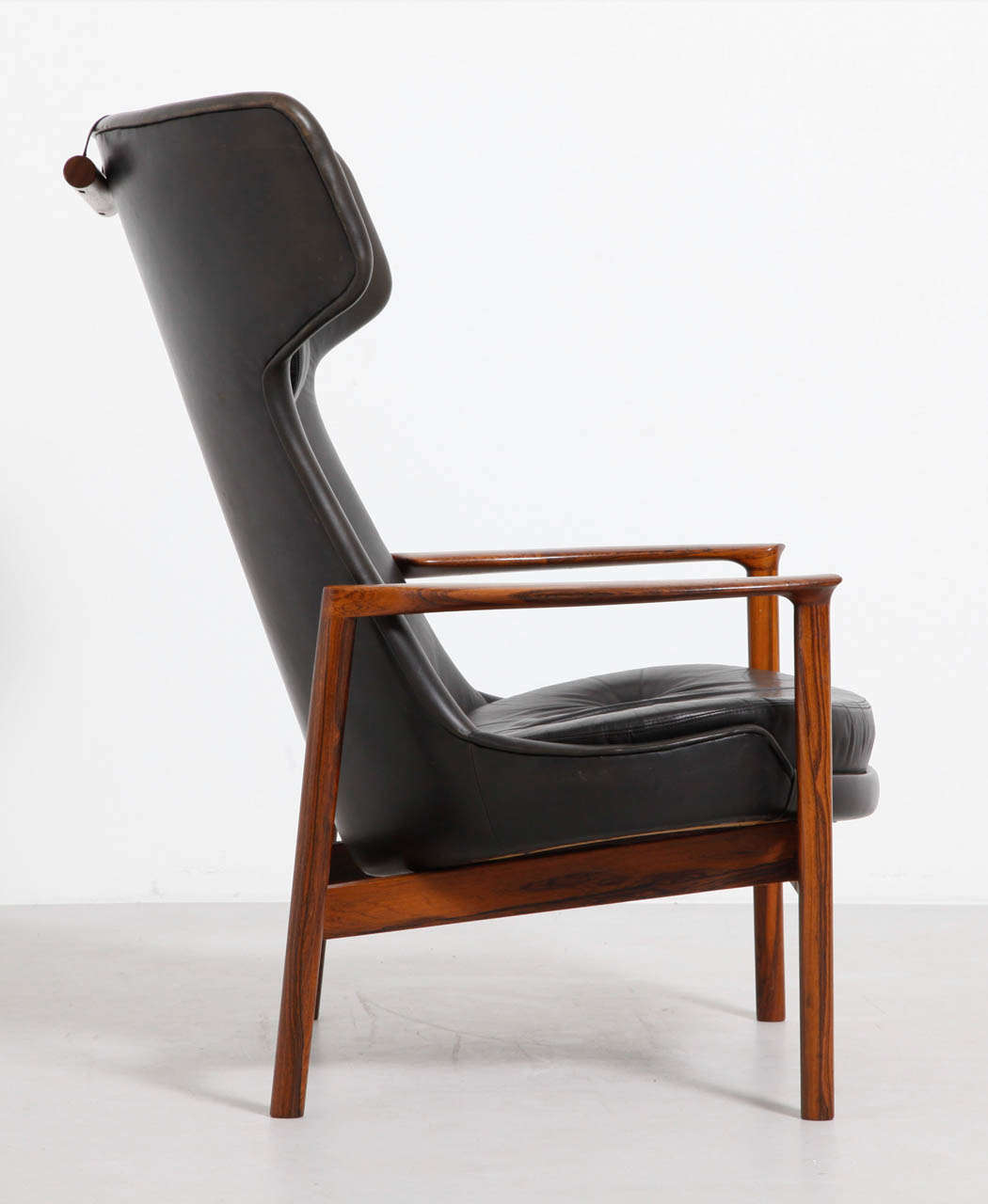 Comfortable walnut wing back chair designed by Ib Kofod-Larsen, 1954, produced by Carlo Ghan Denmark. Original black leather upholstery with a loose cushion and a comfortable cushion to support your head.The frame is beautifully detailed. This is a