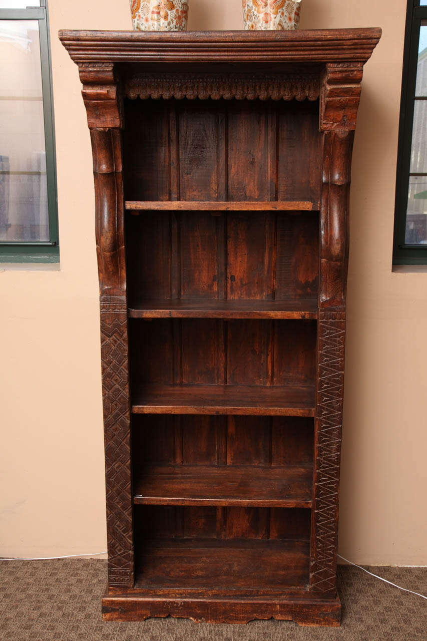 A Javanese tall wooden bookcase with carved side posts and six shelves. This wonderfully detailed bookcase was carved in wood on the island of Java during the 1900s. The bookcase features a beautifully carved cornice over a carved molding. Six