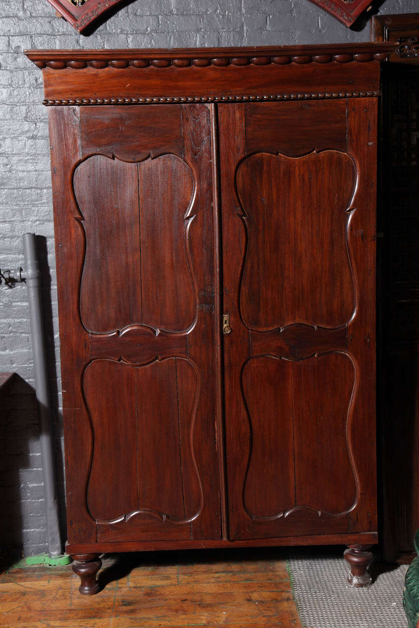 This large 20th century armoire with two carved doors comes from Java, Indonesia. The armoire showcases a massive rectangular shape with two carved doors displaying four rounded panels. The top is adorned with a carved molding with edge patterns