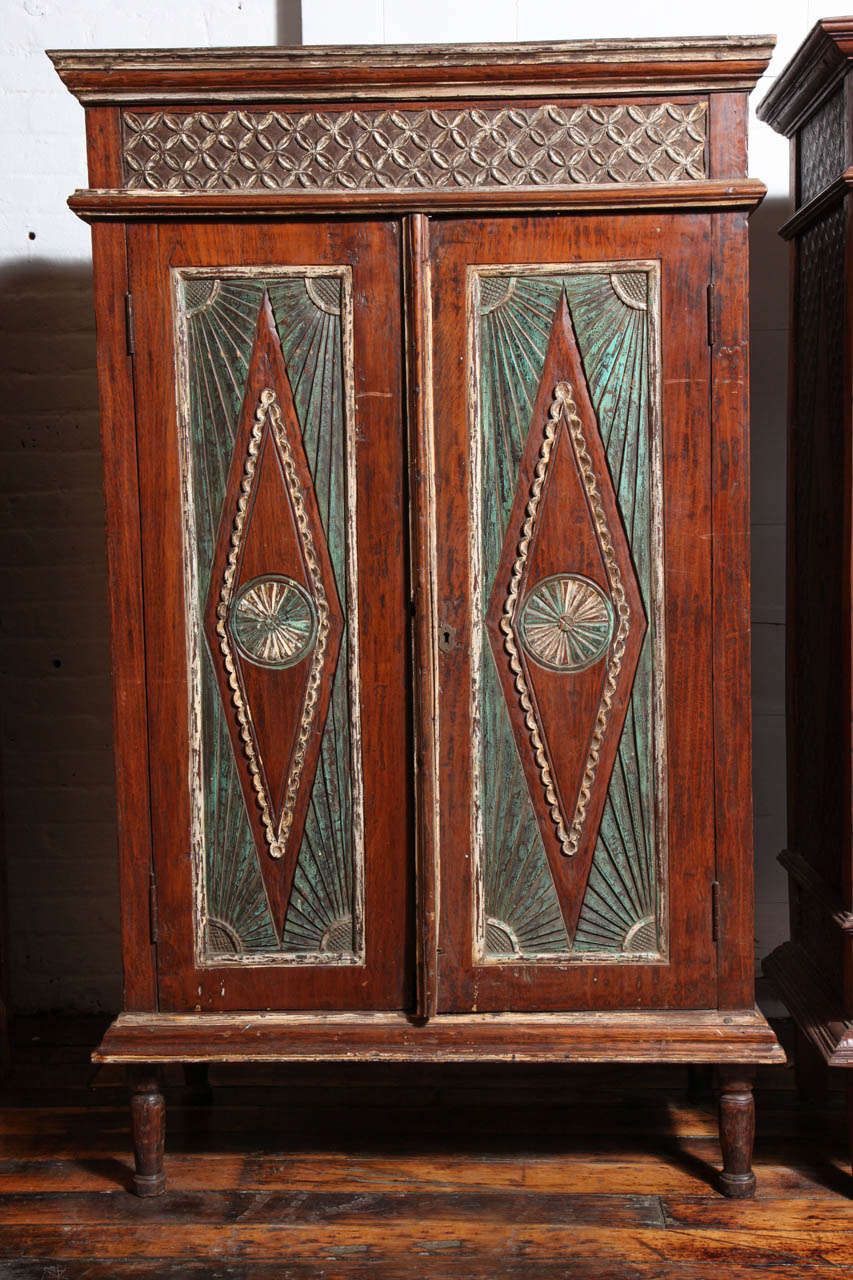 This antique teak cabinet comes from Java, where it was made and painted during the early 20th century. The cabinet features a rectangular Silhouette surmounted by a cornice adorned with carved rosette motifs, accented with white paint. Two carved