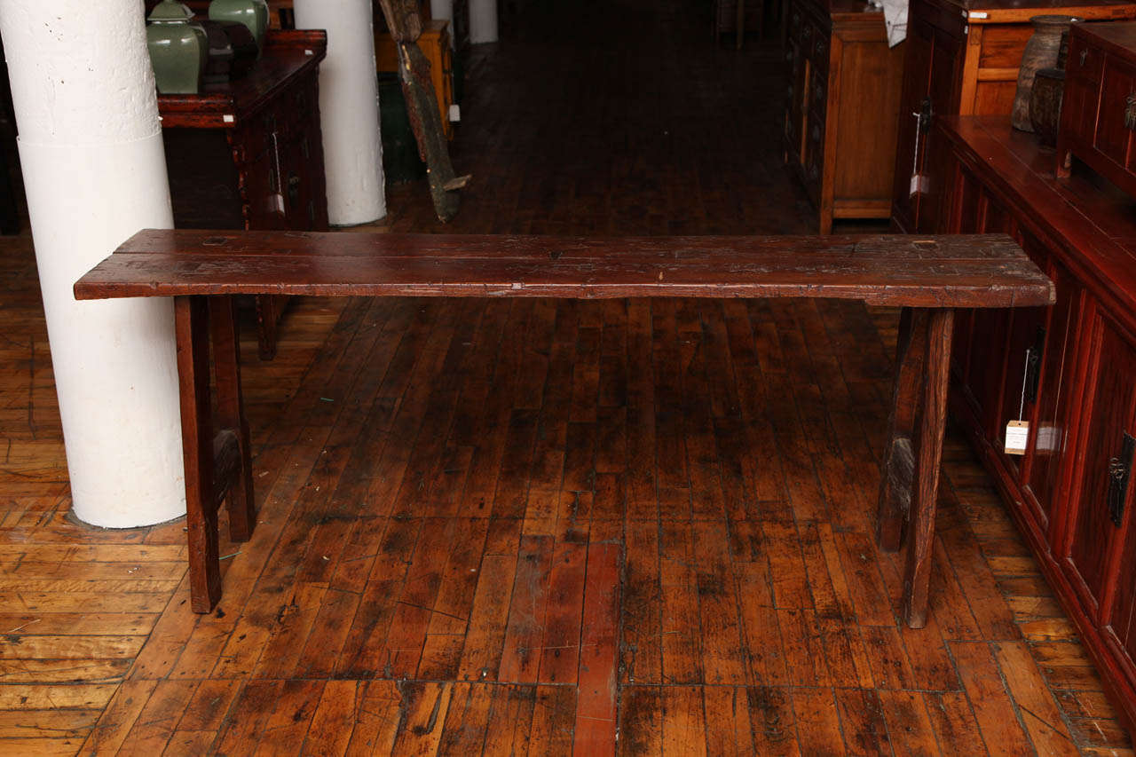 This long and narrow wooden table originates from the Indonesian island of Java, where it was made from a tree during the 19th century. The rectangular top is made of two long planks and sits on two sturdy inset recessed legs. Its simple lines, dark