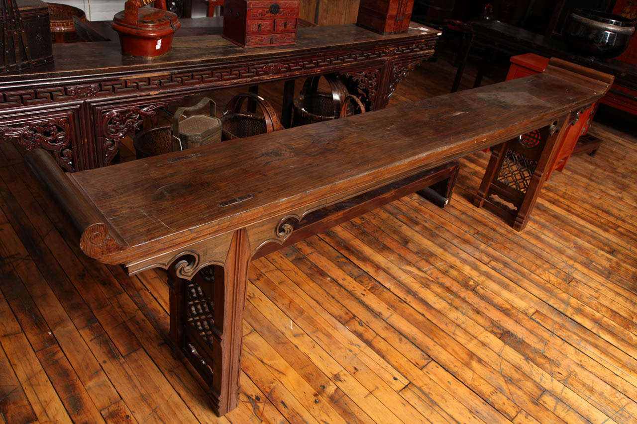 A Chinese 19th century 9 foot long antique altar table with original surface, everted ends, carved spandrels and fretwork designs at the base. This Chinese 19th century long wood console table features its original surface and carved patterns. The