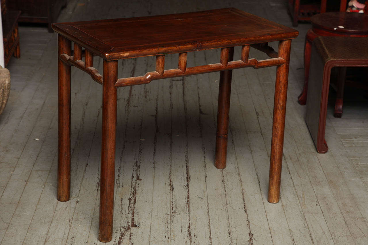 This 19th century Chinese small console or wine table was made with elmwood during the Qing Dynasty (1644-1912). The table adopts a refined shape made with light brown lacquered wood. The four cylindrical legs are surmounted by a top displaying a