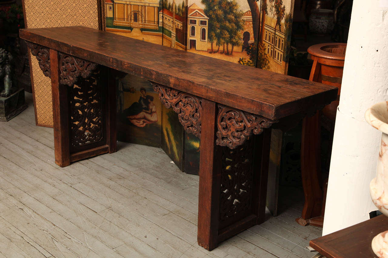 A large palace altar table from 1800s, China. This 19th century Chinese palace altar table was made with carved elmwood. The altar table is varnished with a brown lacquer, which enhances the wood grain. The table displays openwork panels on its