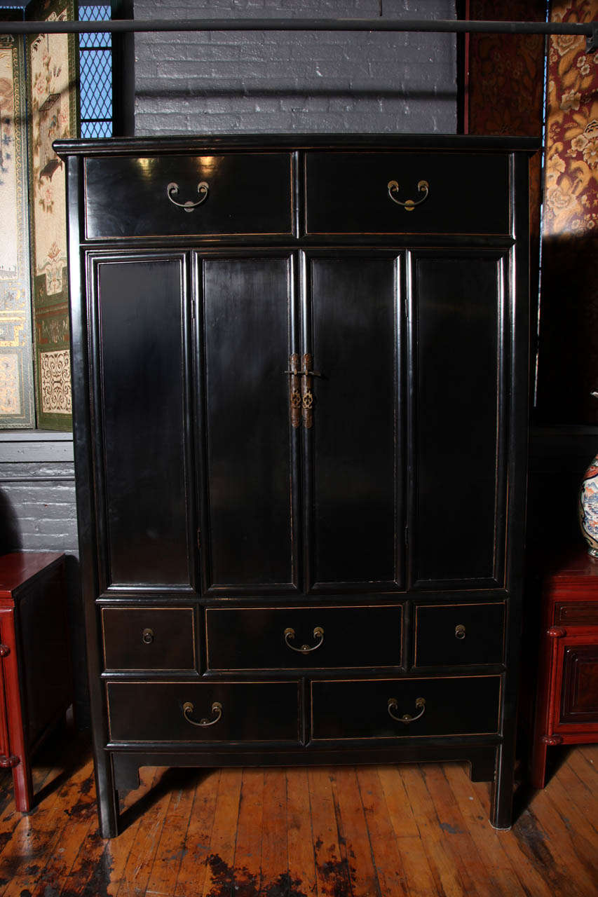 This Chinese 20th century tall chest featuring a double door was made with black lacquered elmwood. The chest showcases a refined rectangular shape with two doors, five large drawers and two small square ones. Each drawer opens thanks to a rounded