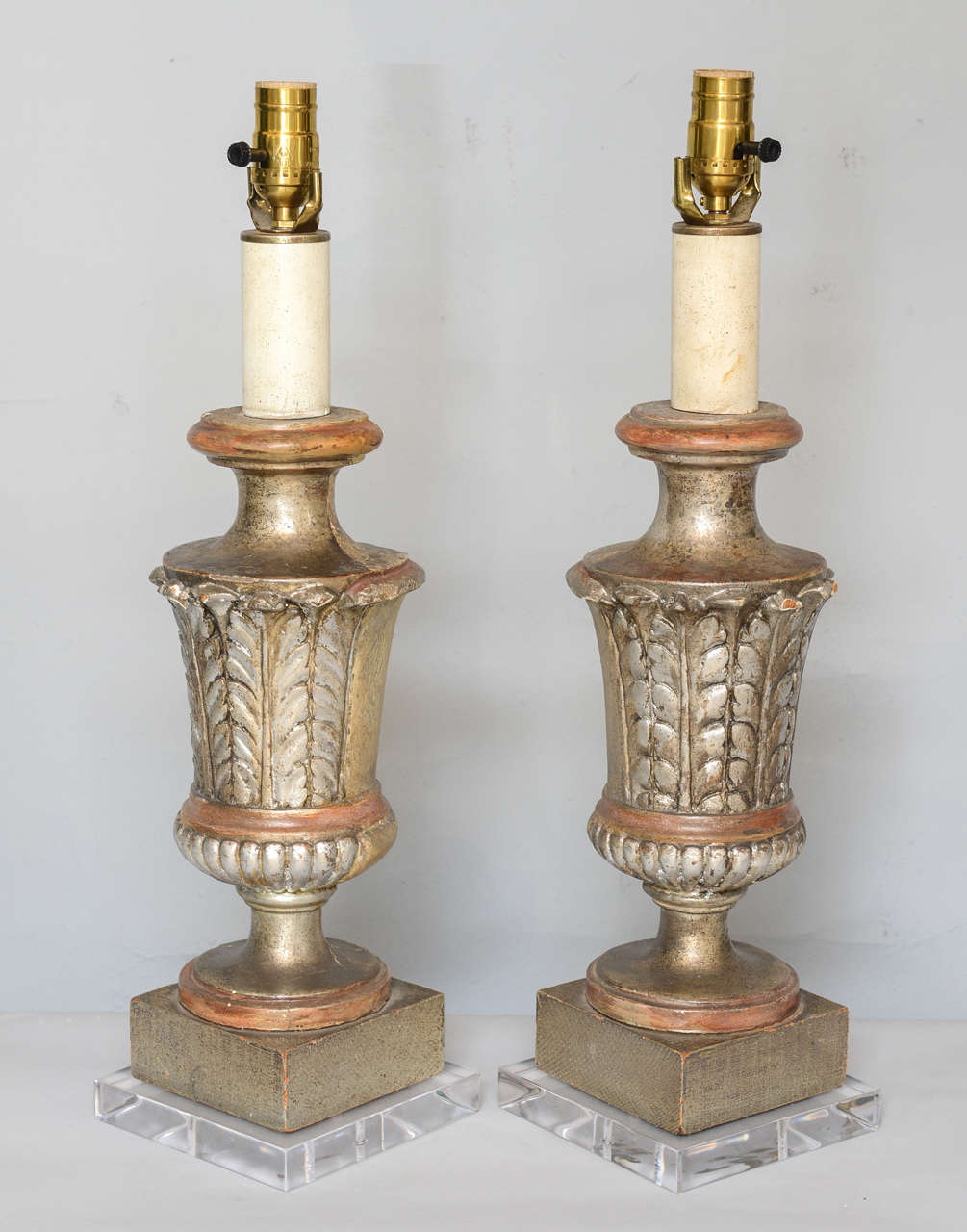 Pair of lamps, each a carved wooden urn-shaped finial, painted and parcel silvergilt over gesso, the front decorated with acanthus leaves, on round foot, lamped on square custom Lucite bases.

Stock ID: D4127