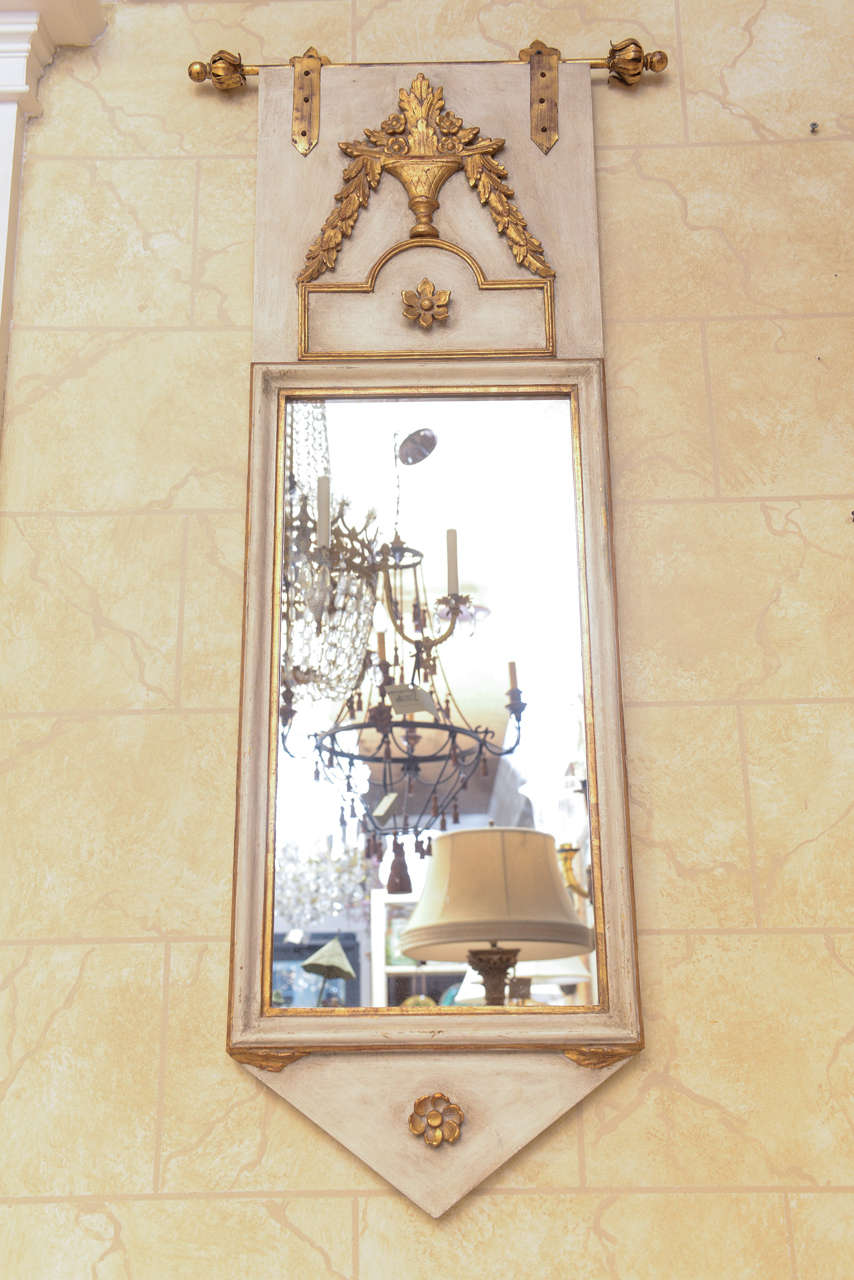 Pair of Mid-Century banner-form mirrors, each rectangular plate in painted and parcel-gilt molded frame, surmounted by carved giltwood flower-filled urn flanked by festooning, a rosette-centered chevron at its base. Each mirror 