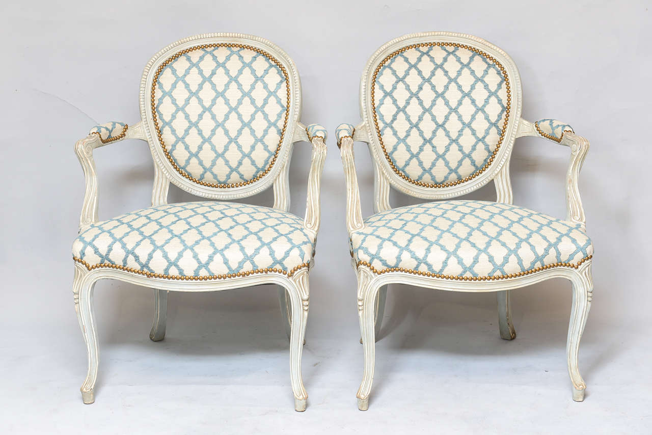 Pair of armchairs, each having a painted frame with natural wear; its round padded back with dentil border carving, ouswept arms with elbow cushion ending in scrolls, on sweeping terminals, to its crown seat and bowed seatrail, raised on tapering