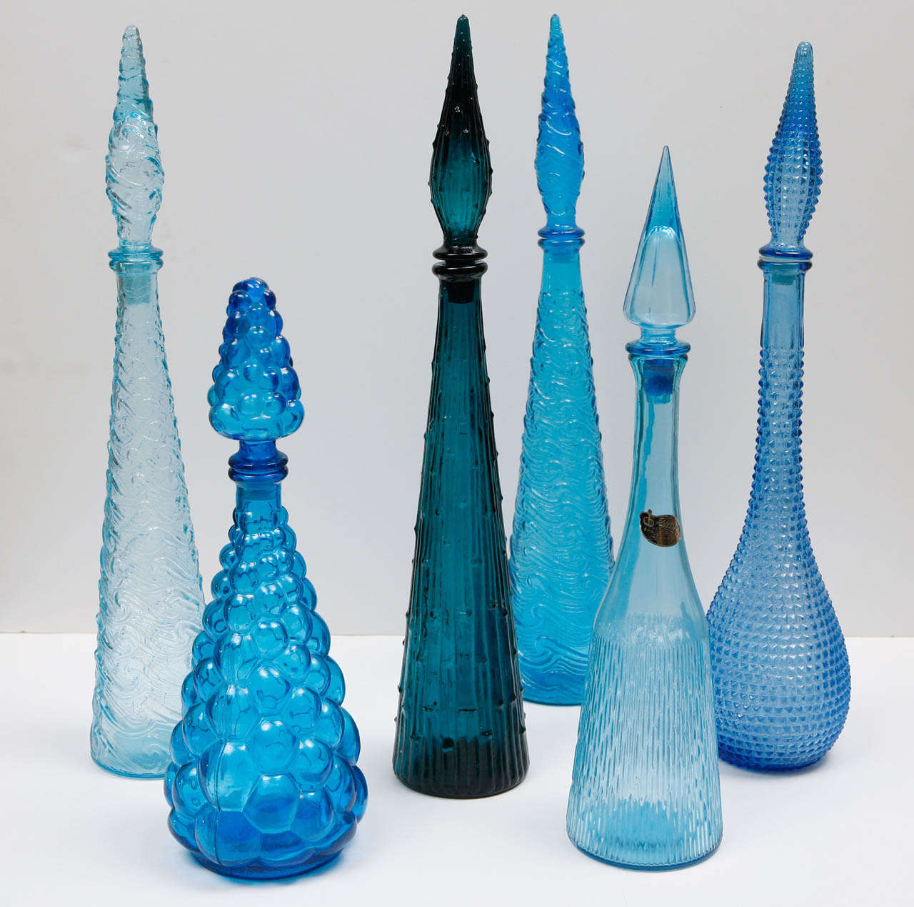 Murano bottles with stoppers that are various shades of blue and heights.